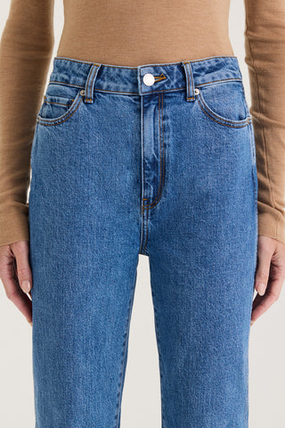 Close up view of models waistband wearing indigo wash high rise, straight leg jeans on a white background
