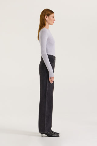 Side view of a model wearing black wash straight leg and high rise jeans with a grey long sleeve top on a white background.