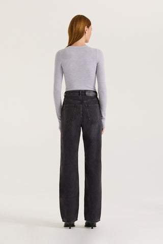 Back view of a model wearing black wash straight leg and high rise jeans with a grey long sleeve top on a white background.
