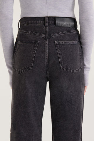 Close up back view of model wearing black wash straight leg, high rise Jeans with a Henne leather patch on a white background