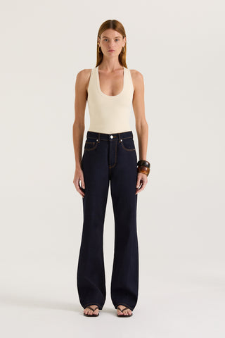 Model wearing dark indigo straight leg and high rise jeans with a cream tank top on a white background